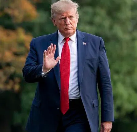 Donald Trump in a dark suit and red tie raising one hand