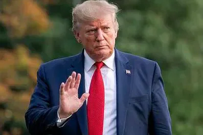 Donald Trump in a dark suit and red tie raising one hand