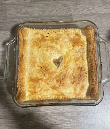 A baked chicken pot pie in a glass dish with a small heart-shaped decoration