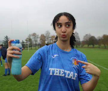 A player in a blue shirt holding a water bottle on a football pitch.