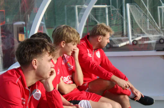 Players in red kits seated in a dugout.