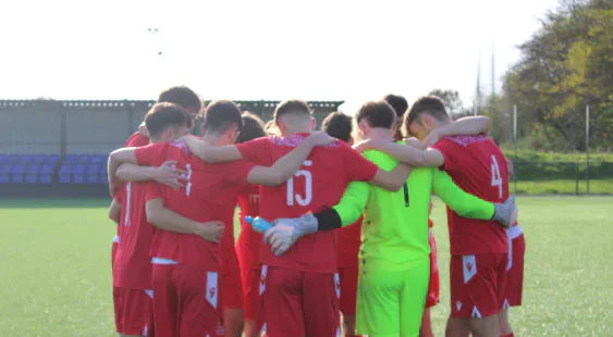 A football team in red kits huddling on the pitch.