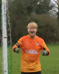 A goalkeeper in an orange shirt beside a goal.