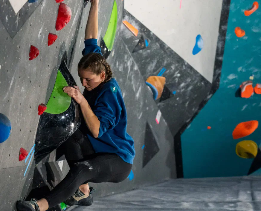 A climber reaching for a hold on an indoor climbing wall.