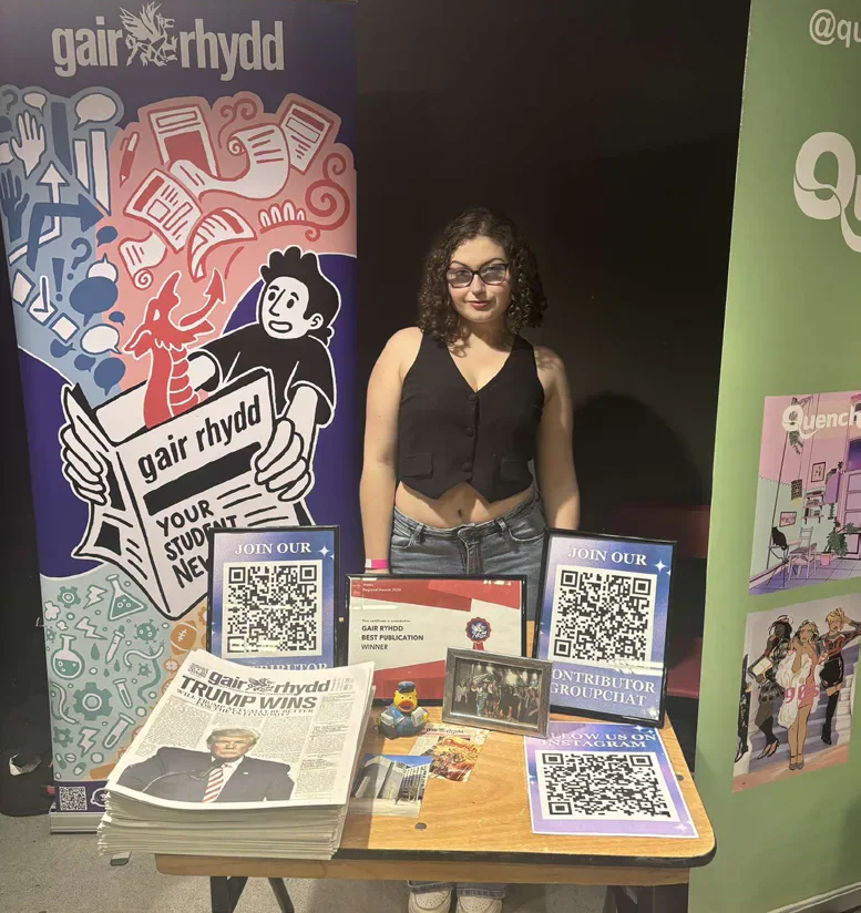 A person behind a Gair Rhydd display table with newspapers and promotional material.