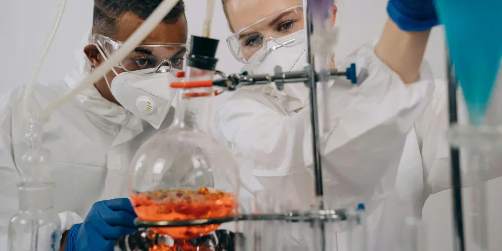 Two researchers wearing protective equipment working with laboratory glassware