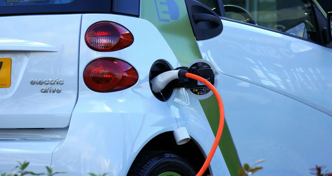 An electric car connected to an orange charging cable.