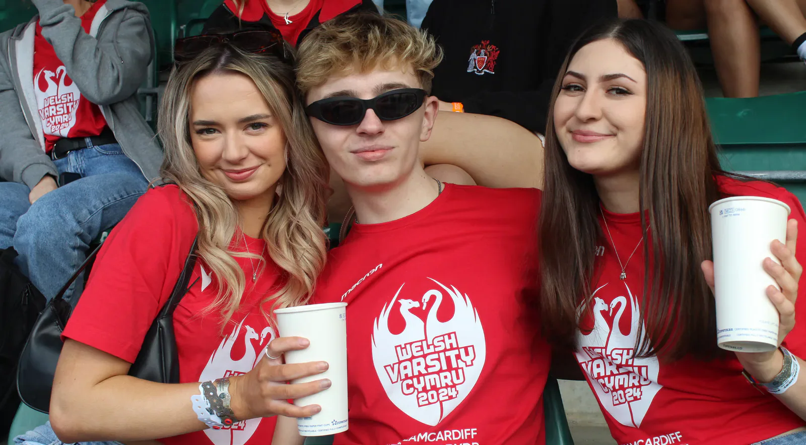 Three spectators wearing red Welsh Varsity shirts in the stands.