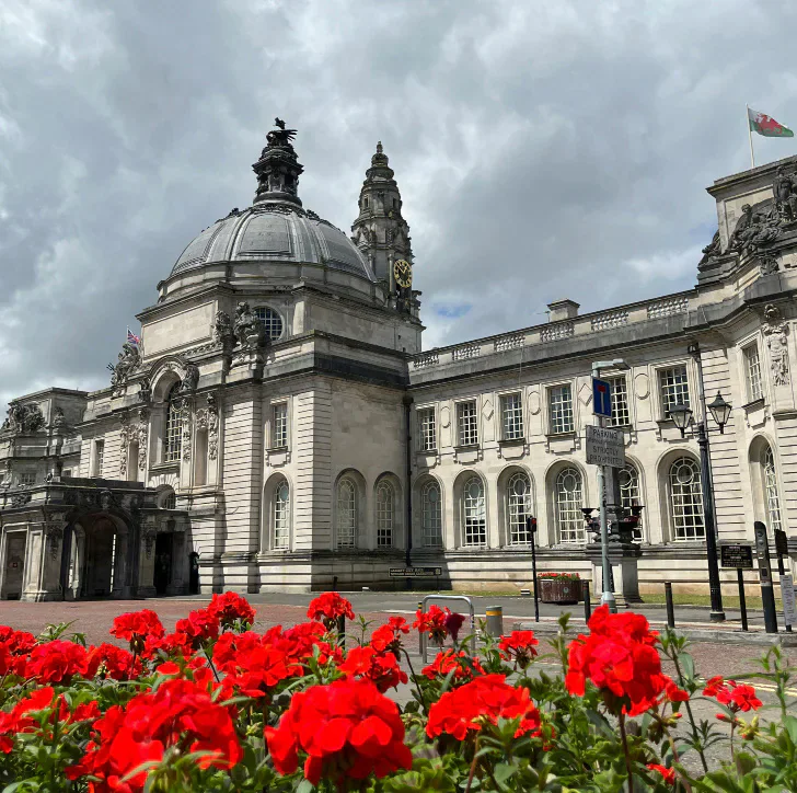 A domed civic building with red flowers in the foreground.