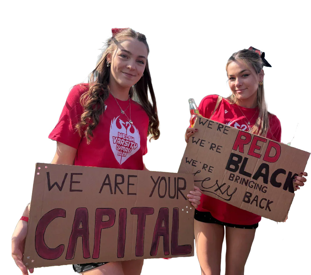Two Cardiff supporters in red shirts holding handmade signs at Welsh Varsity.