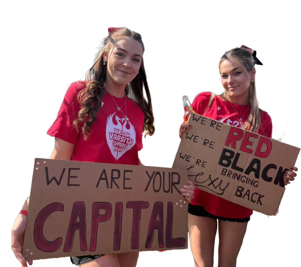 Two Cardiff supporters in red shirts holding handmade signs at Welsh Varsity.