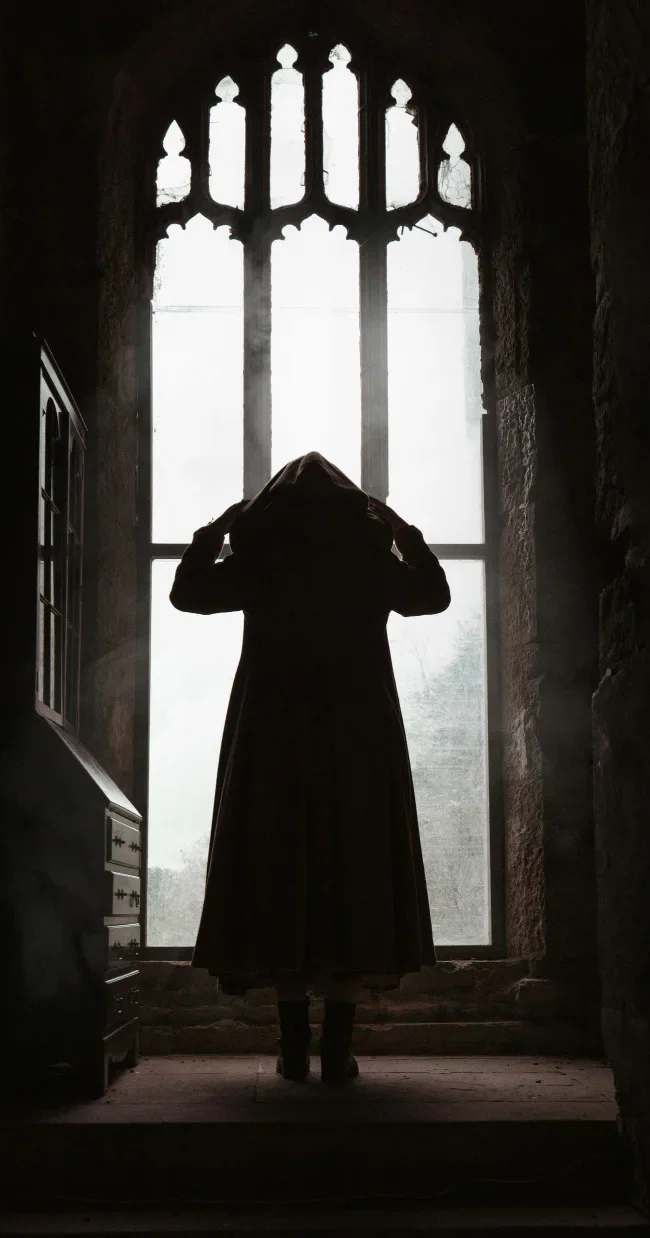 A silhouetted figure standing before a tall Gothic window.
