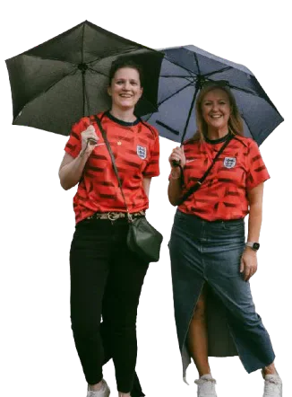 Jess Fishlock and another Wales supporter wearing red beneath umbrellas.