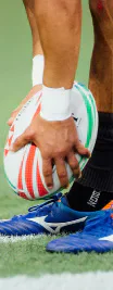 A rugby player with taped wrists holding a ball above the turf.