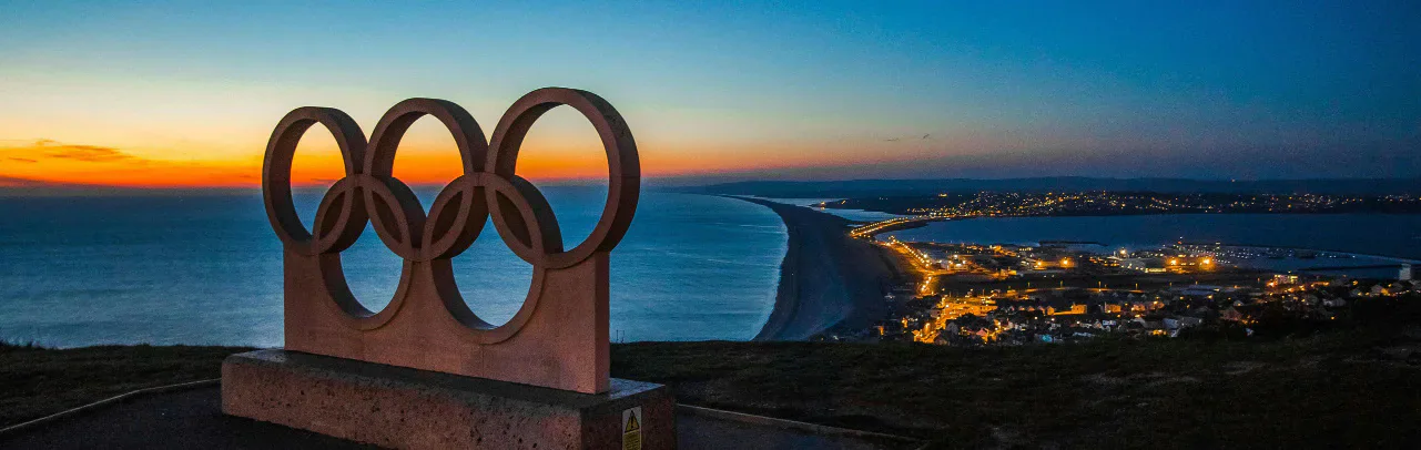Olympic rings monument overlooking a coastline at sunset.