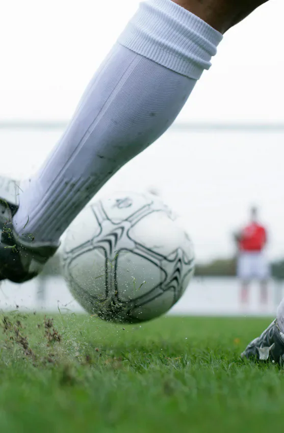 A footballer in white socks kicking a ball on grass.