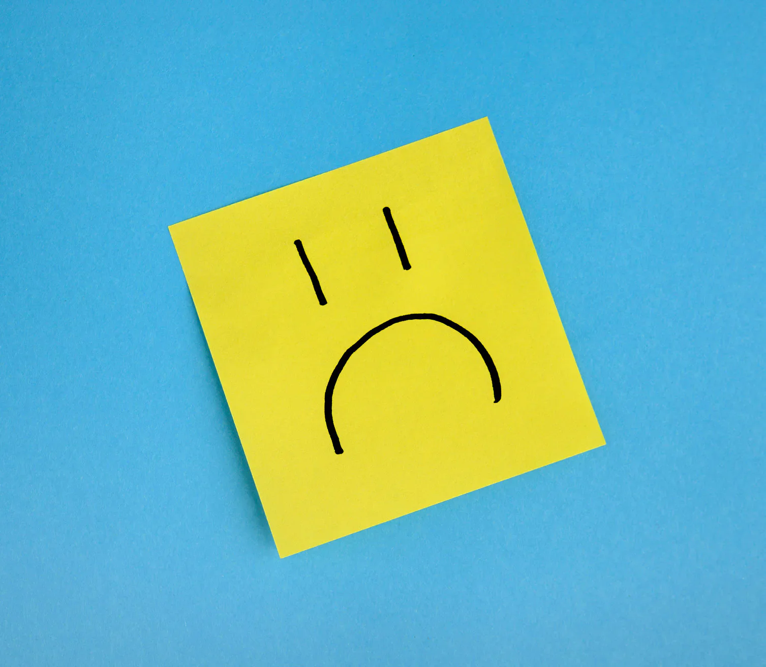 Yellow sad-face sticky note on a blue background.