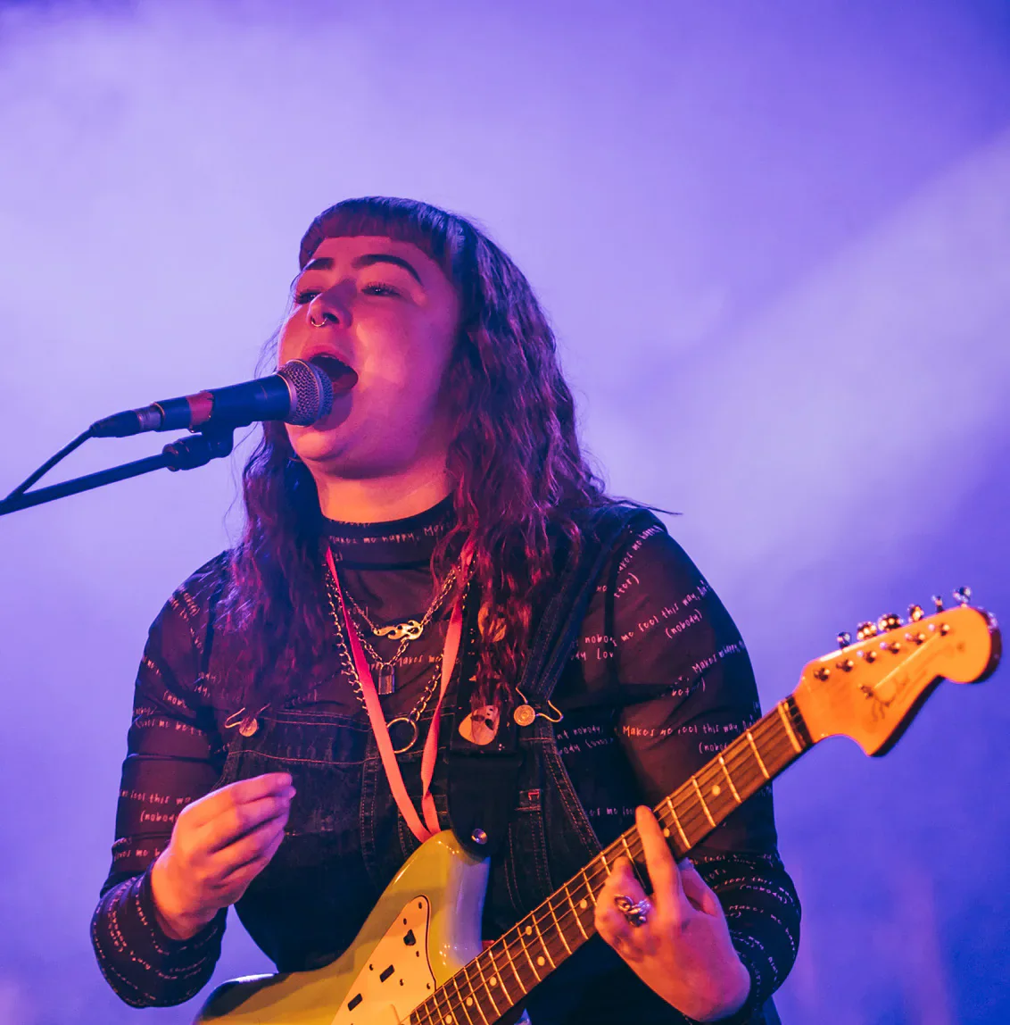Welsh musician singing and playing electric guitar under purple stage lights.