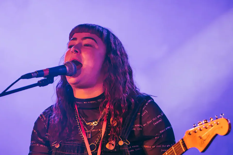 Welsh musician singing and playing electric guitar under purple stage lights.