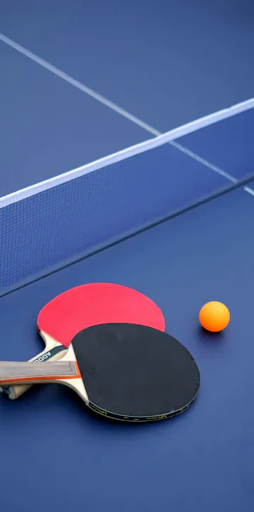 Table-tennis paddles, ball and net on a blue table.