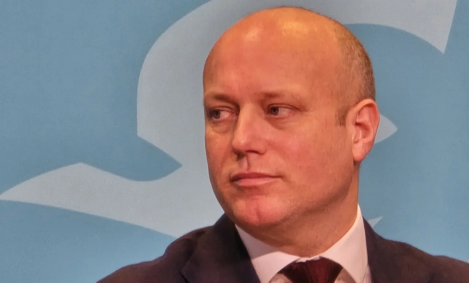 Dan Thomas speaking against a pale blue backdrop