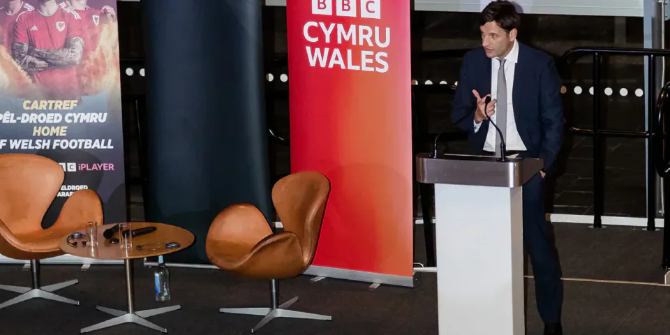 A Welsh football anniversary event with a speaker at a lectern