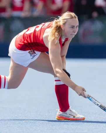 A Cardiff hockey player in red and white reaches forward with her stick on the blue pitch.