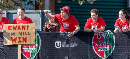 Cardiff supporters lean over Varsity banners beside an Ewan you will win sign.