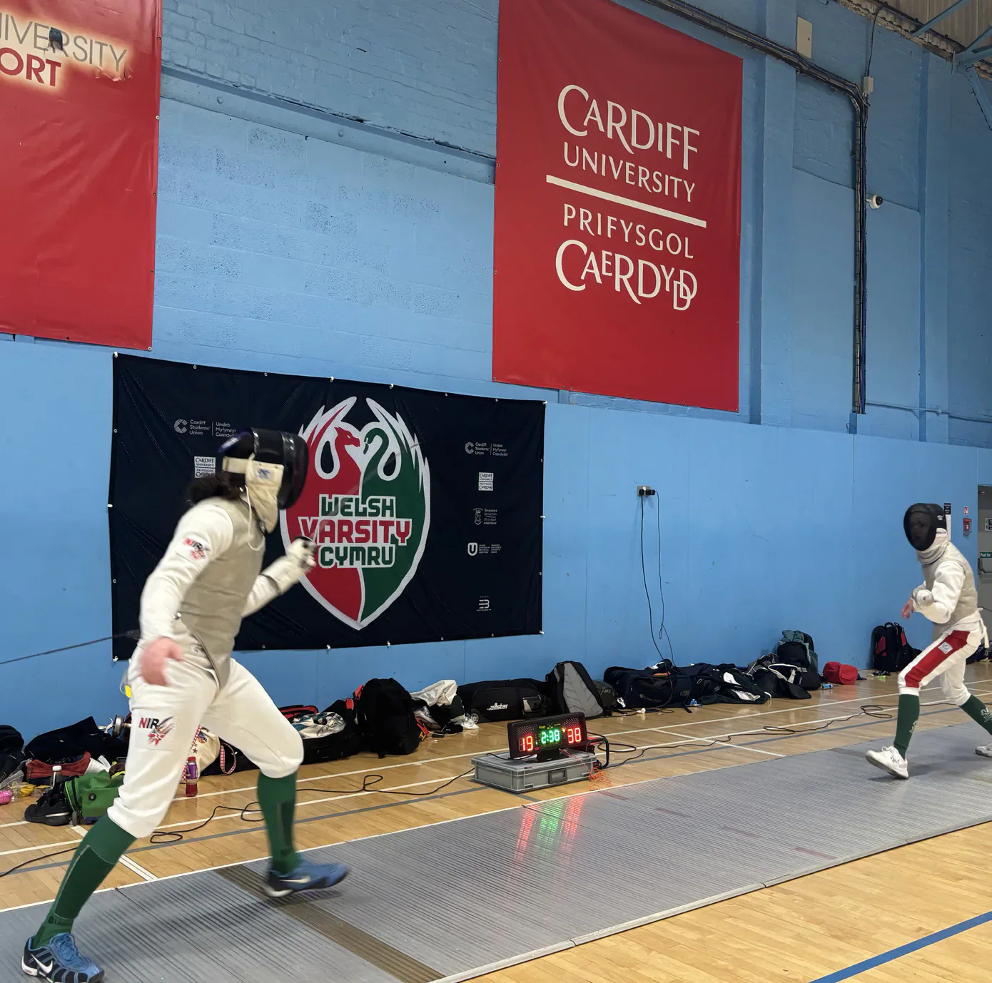 Two fencers face each other beneath a Cardiff University banner.
