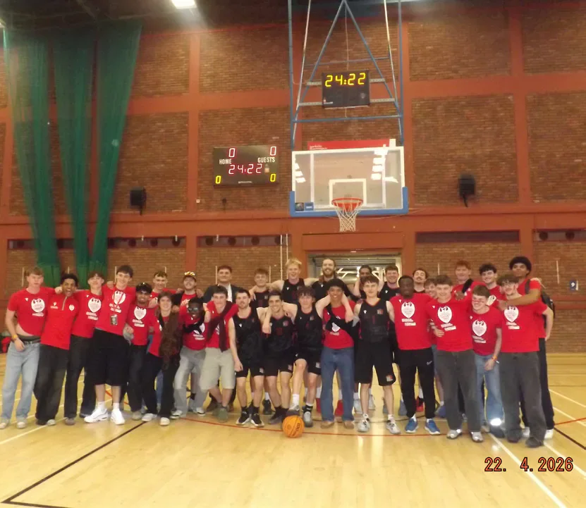 The basketball team and supporters pose together beneath the hoop.