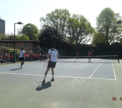 A tennis player stands ready on court with spectators behind the fence.