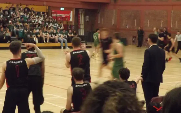 Cardiff basketball players and a coach watch from the sideline.