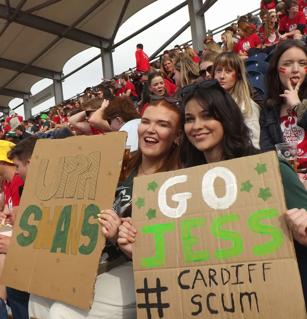 Spectators hold handmade support signs in the cricket stands.
