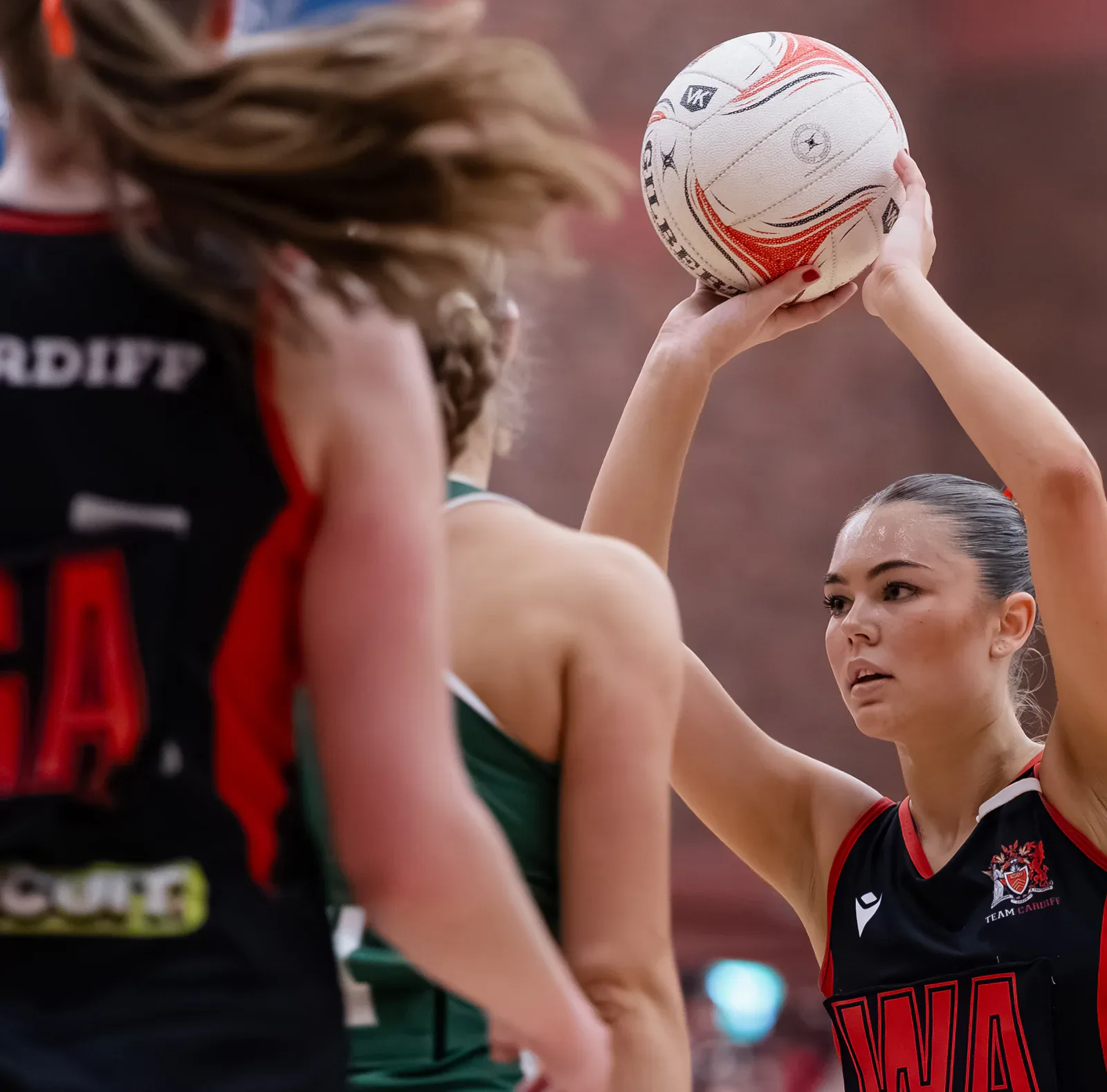A Cardiff netball player prepares to shoot while Swansea players defend.
