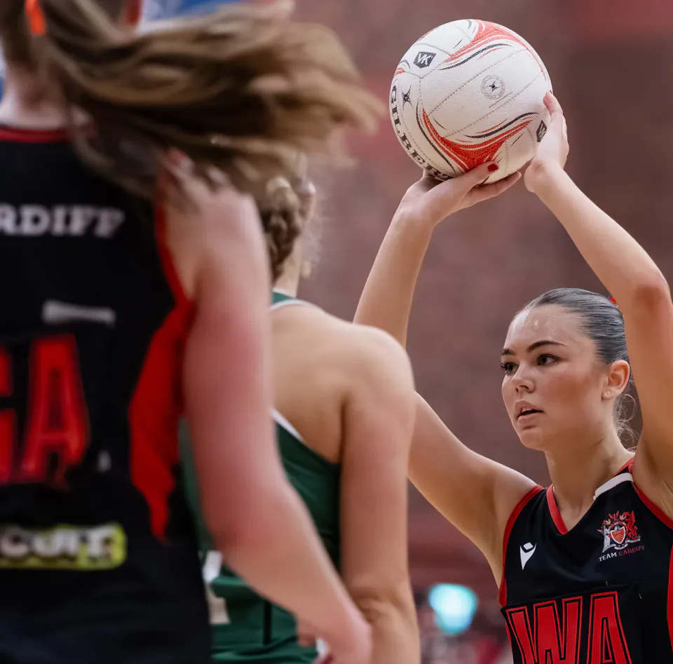 A Cardiff netball player prepares to shoot while Swansea players defend.