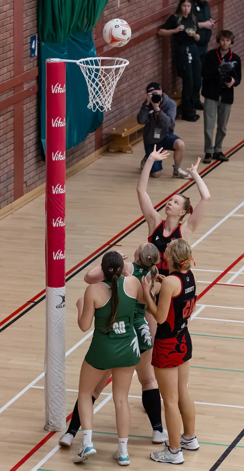 Cardiff and Swansea netball players watch a shot above the basket.
