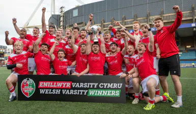 The Cardiff rugby team celebrates behind a Welsh Varsity winners banner.