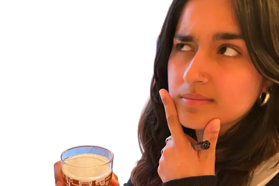 A person holding a pint and resting a hand against their chin.