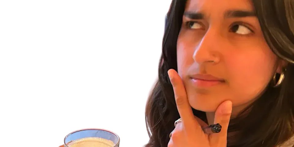 A person holding a pint and resting a hand against their chin.
