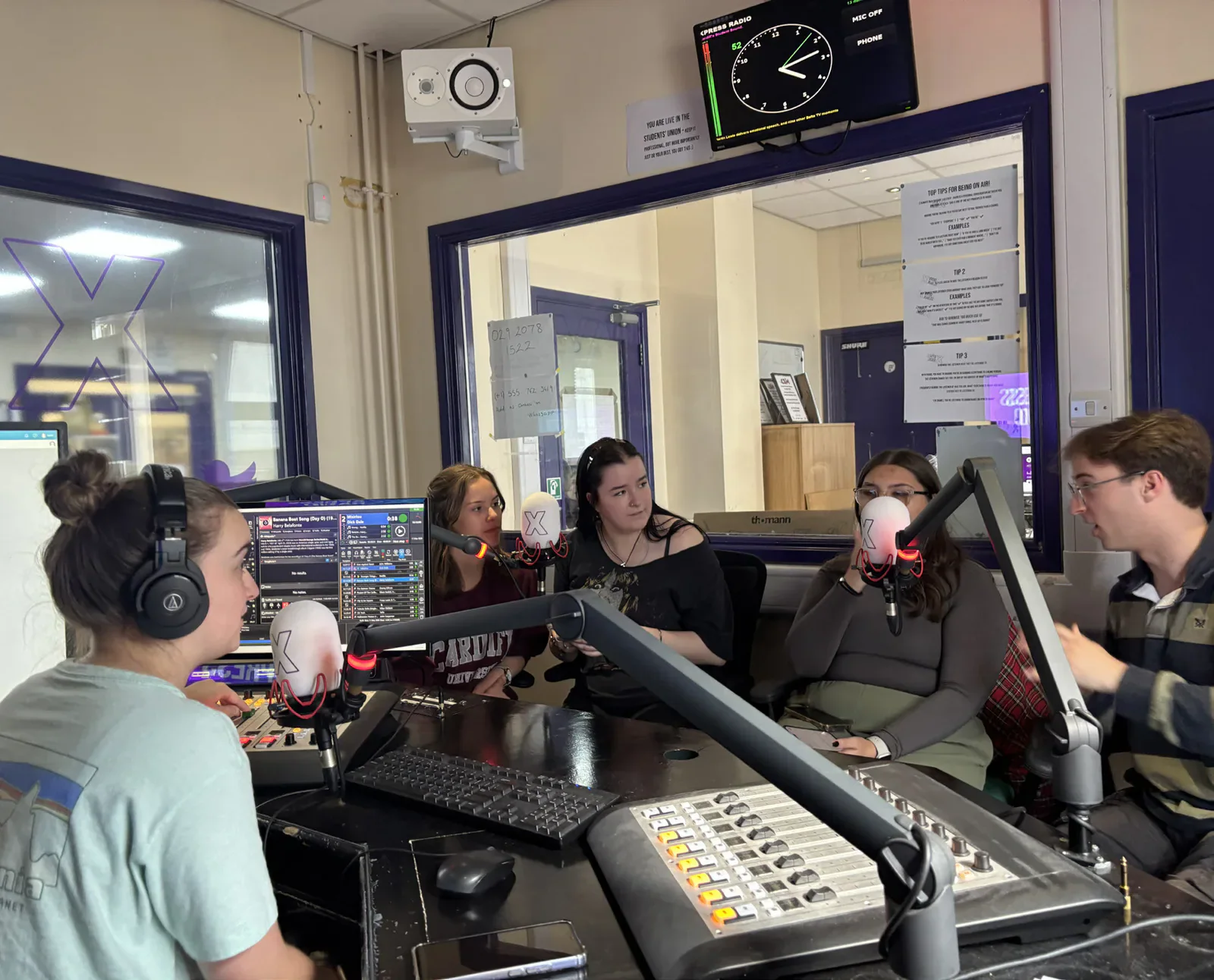 Five people seated around microphones and a mixing desk in the Xpress Radio studio.