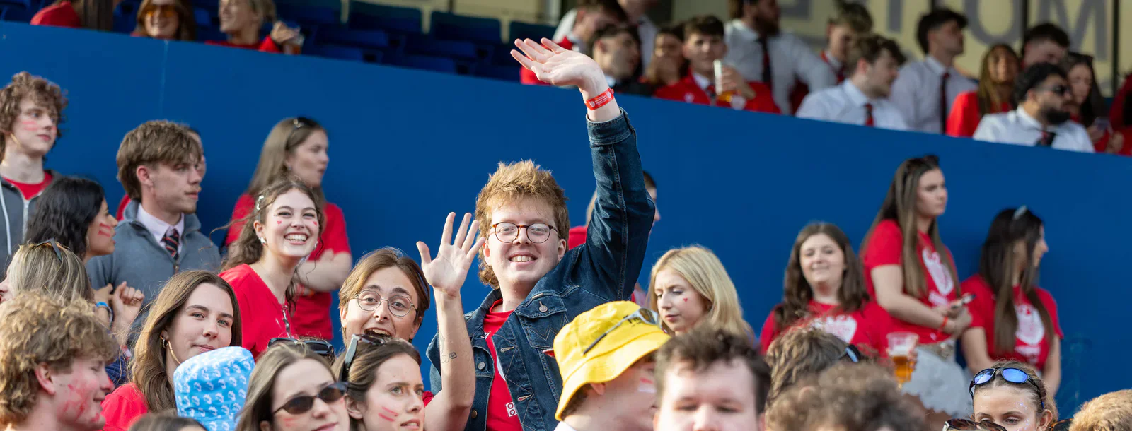 A spectator raises one hand above a crowd beside blue railings.