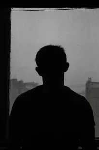 Silhouette of a person looking through a barred window.
