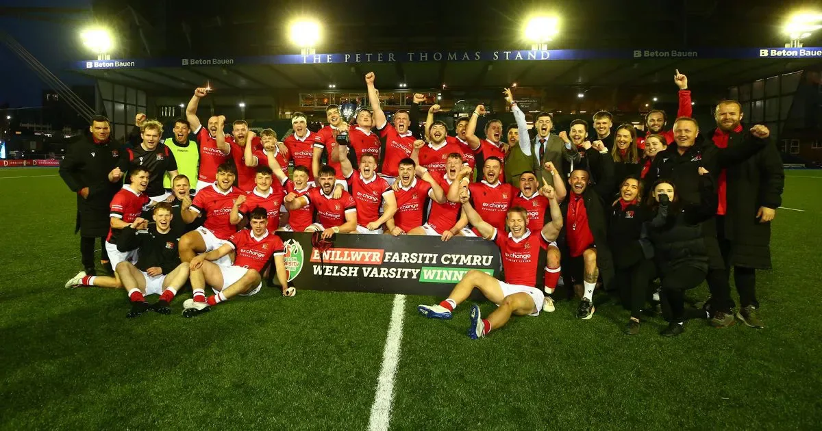 Cardiff rugby players and staff celebrate with the Welsh Varsity winners banner at Arms Park.