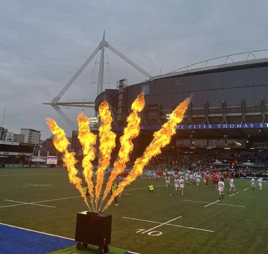 Flames rise beside the Arms Park pitch as rugby players enter the field.