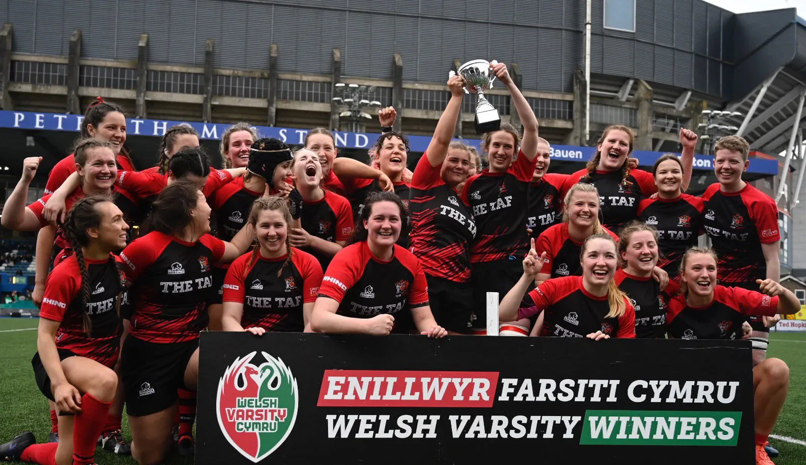 Cardiff women celebrate with the rugby trophy and Welsh Varsity winners banner at Arms Park.