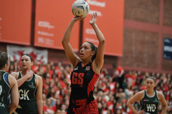 A Cardiff netball player holds the ball above her head as Swansea players defend.
